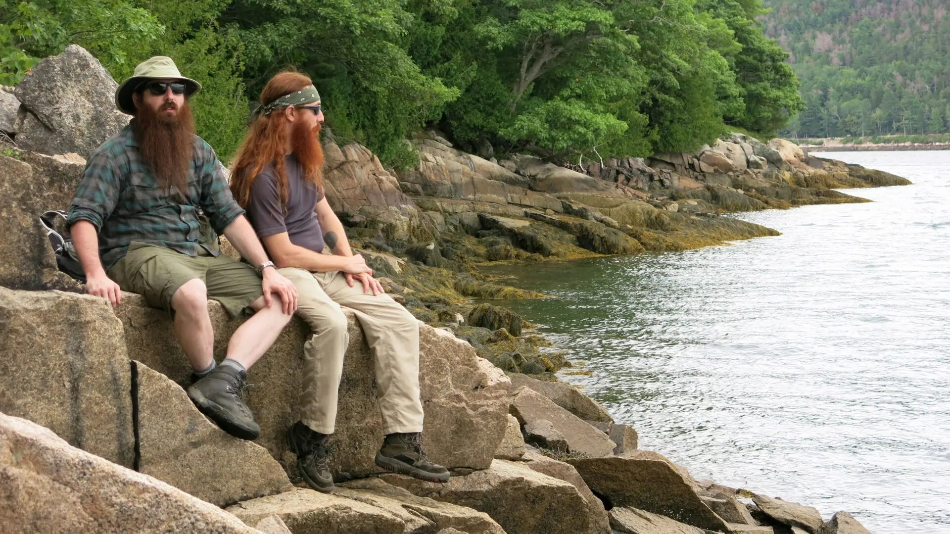 Two people sitting on rocky shoreline.